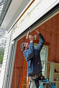 The door hangs from the top rail so it needs to be securely fastened to the header. This is a two-step process, beginning with predrilling the header for lag screws through the holes in the top rail provided by the manufacturer.