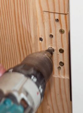 Supporting the open door on a wedge, the author folds back the hinge leaf, drills out the offending hole with a countersinking bit.