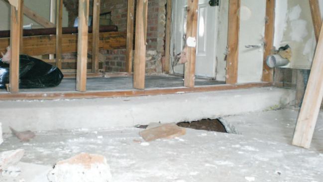 With the drywall stripped from the laundry-room and family-room walls, the sag in both slabs is evident. Note the inspection hole in the concrete.