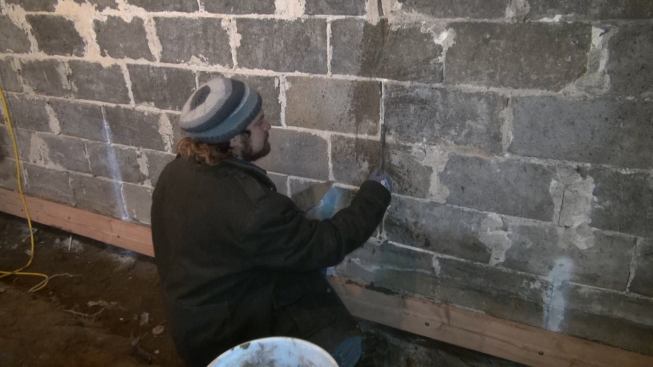 Martignetti works grout into the crack. The entire face of the block foundation will later receive a reinforcing parge of modified cement.