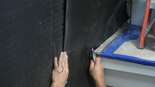 The crew trims the Sound Barrier HD in place with a razor knife. A close fit is important for the material to perform effectively.