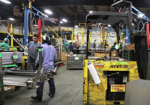 This is the flow line cell where Storagemaster chests are assembled. Pieces are tacked (spot-welded) in place and then the weld is completed at the next station down the line. 
Click here for video. My tour guide frequently spoke of ergonomic adaptations—that the factory is set up to minimize lifting and material handling by humans. Note the red and yellow “tubes” that hang from booms in the background—more on them in the next slide…