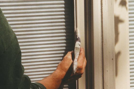 Using a 3 1/2-inch angled sash brush, the author laps the paint slightly onto the glass, creating a final barrier against water intrusion.