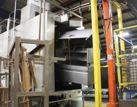 This fully welded box has been hung from an overhead conveyor and is entering the machine that will wash it prior to powder coating. Akin to an industrial dish washer, the machine is about the size of a semi-trailer.