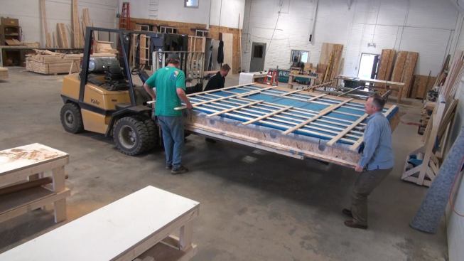 Shop manager Steve Greenleaf, owner Chris Corson, and designer Mike Maines roll a completed panel off the framing table onto the forks of a forklift. The framing table is now ready for the next panel, but Greenleaf still has to finish a few details on this piece of wall.