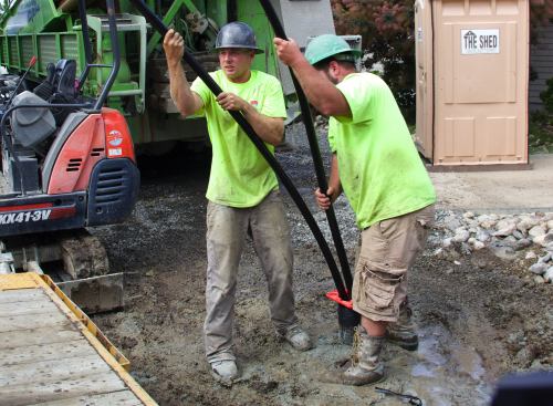 As the air-filled plastic tubing descends into the groundwater-filled well shaft, flotation becomes an issue and the crew has to fight against the buoyancy of the tubing. At that point, the crew connects the tube to a water spigot and fills the tubing with water to eliminate the buoyancy and equalize the weight, allowing the tubing to descend more readily into the shaft.