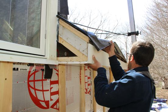 Pollard and Fenton position the fascia for installation. The roofing membrane was intentionally left long in order to be trimmed later to seal the rafter bays against the elements.