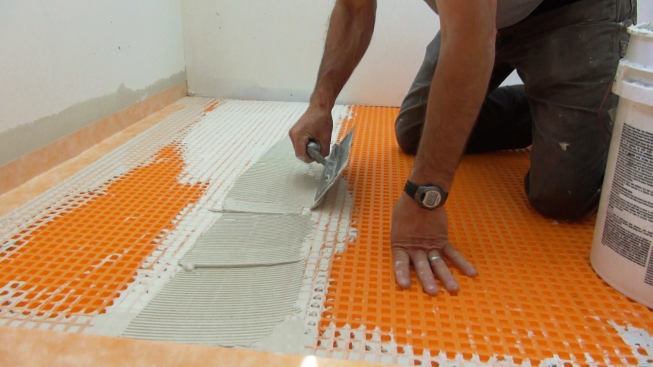 Boucher applies a mortar setting bed at the joint between two sheets of Ditra underlayment. Note: the white mortar already in place at the joint was placed the day before and has hardened overnight. This is a way to use up small quantities of extra mortar so the material won't be wasted, Boucher explains. The fresh mortar will still bond strongly to the previously placed and hardened material.