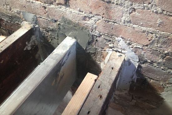 Here, a steel C joist is embedded into the brick party wall dividing the row house from the adjacent unit. The existing brick is more than adequate to support the floor and roof loads involved in the renovation. However, the wall is only 2 wythes of brick thick, and is shared with the neighboring home, so work must proceed carefully. Workers remove enough bricks to create a space to insert the new joist, then work non-shrinking grout into the cavity to support the joist end.