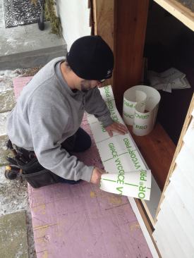 Manny unrolls the length of flashing tape that he pre-cut for the sill. He presses the tape into the corner and marks the location of the corner cuts.