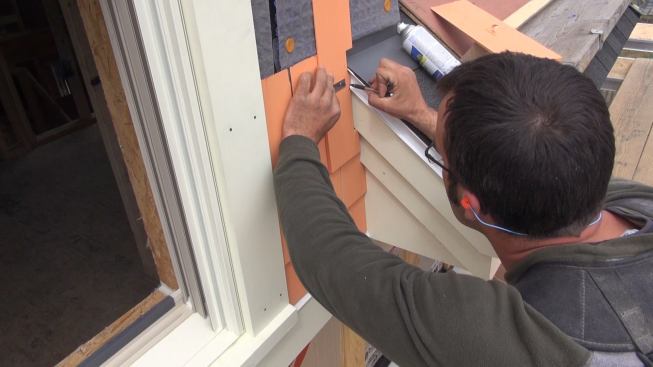 Pollard scribes a wood shingle to fit the profile of the roof trim and metal drip edge. The shingles are factory-dipped with a three-coat finish (one primer coat and two topcoats).