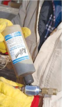The author puts Kilfrost, a synthetic de-icer and lubricant, into an oiler at the end of a hose that will connect to a gun.