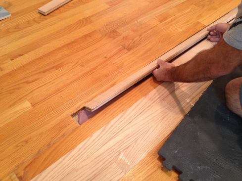 In order to be able to slip the final piece into place, Manny rips off the bottom of the groove. He then slips the tongue of the new board into the groove of the existing floor and taps it flat. It can help to plane or rip a slight bevel on the upper part of the groove to help it slip in.