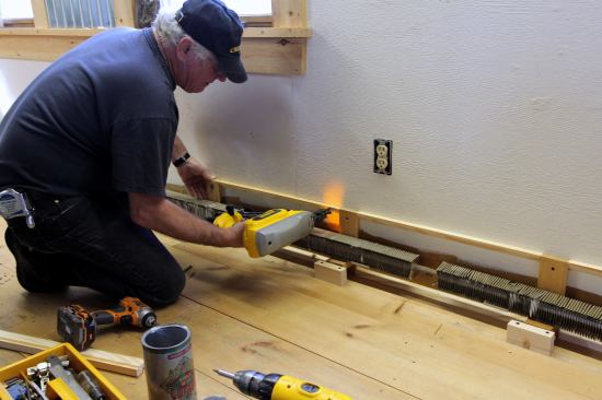 With the base blocks screwed to the floor for the front of the cover, strips of wood with a ripped bevel set the space between the brackets at the back against the wall. The base blocks then attach to the brackets from the front.