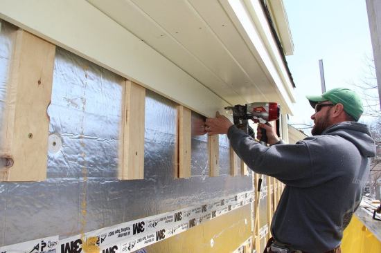 Fenton nails the frieze board over the plastic vent and 1x4 furring. The top edge of the clapboard siding will slide into the gap between the frieze and the 1x4's, leaving a 3/8-inch gap for the exhausting air.