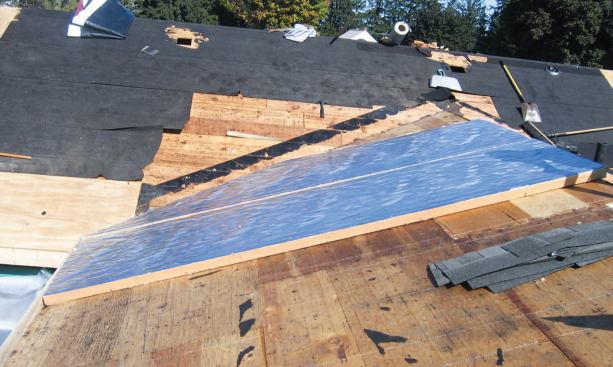 Foil-faced polyiso board, screwed to the addition roof deck, supplements the original batts, which were left in place between the rafters. Joints between panels — and the intersection with the board deck of the original house, visible at rear — were sealed with spray foam.