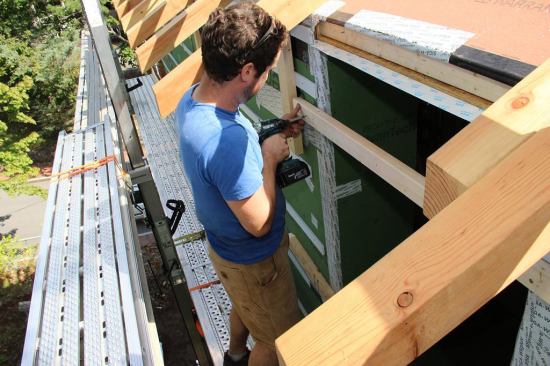 Operations Manager Evan Smith screws a temporary rail over the window opening to keep the window in place for leveling, squaring, and fastening.