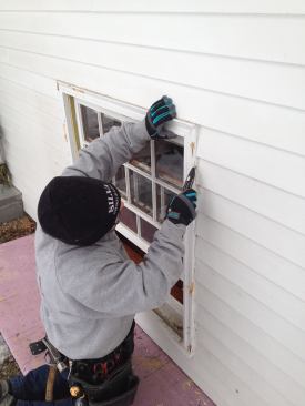 Once outside he slices back the caulking between the window and the clapboard siding.