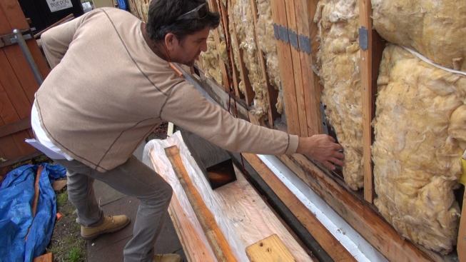 Gregor pulls back insulation in the outside wall to reveal another hold-down, part of the beefed-up structure for the long front-to-back exterior walls of the bungalow.