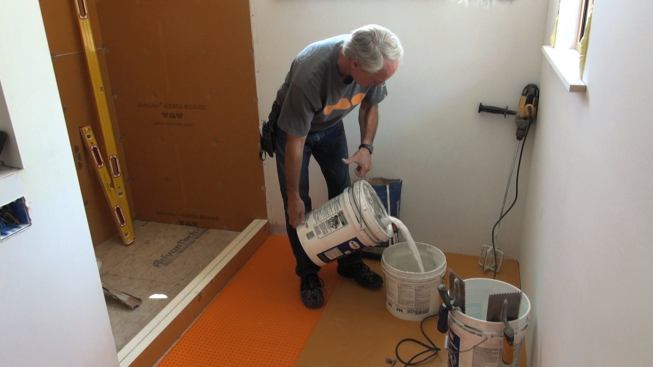 Boucher used unmodified mortar to join the two pieces of the curb together. Here, he mixes up a small batch of modified mortar, using latex additive, for adhering the curb to the engineered wood panel subflooring. Unmodified mortar is used whenever impervious layers are laminated together; modified mortar is used when the wet mortar will have the ability to dry by evaporation or absorption (in this example, over the Advantech subfloor).