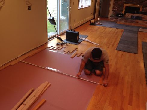When all the pieces have been stripped and staggered back, Manny puts down an underlayment of red rosin paper (to help reduce the chance of squeaks between the hardwood and the subfloor). He then sets his starter strips in place temporarily measuring back to the existing floor to keep them parallel.
