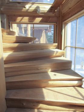 Each individual cedar tread is the full thickness of a riser; the natural curvature of the slab edges provides the code-required nosing. A custom iron railing, not yet installed, will protect the adjacent windows.