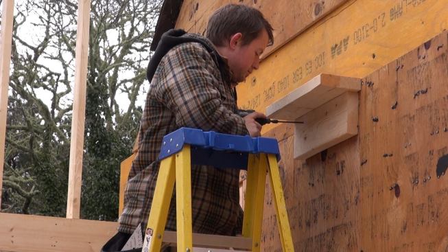 Carpenter Russ Laffin sets a temporary shelf to catch the end of a built-up two-ply LVL beam for the floor frame of a second-story loft under the cathedral ceiling of a high-performance addition on Cape Cod.