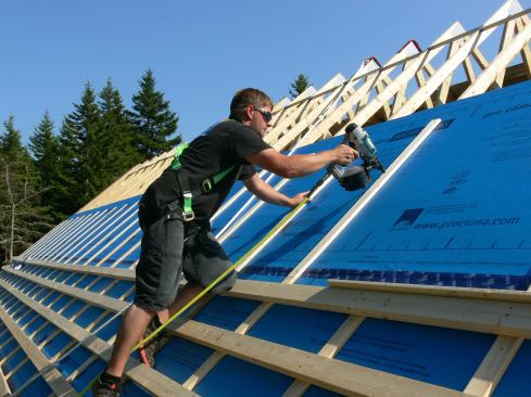 Using the lower courses of 2x4 cross-strapping for footing, a carpenter extends the vertical 1x3 strapping farther up the roof, working towards the peak.