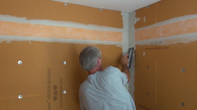 Pressing gently to avoid snagging the already placed horizontal Kerdi membrane, Boucher applies mortar to the wall corner and tools it with the short notched end of the Kerdi one-eighth-inch trowel.