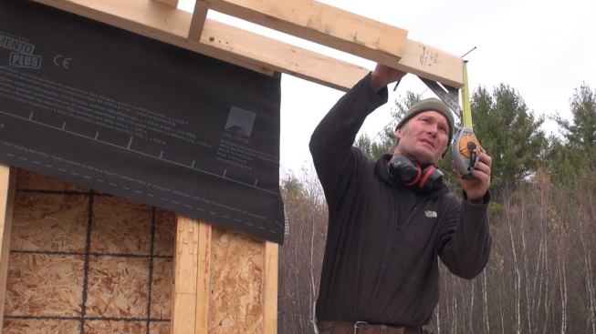 Kruse measures the rafter tail and ponders the layout for the fascia and soffit framing at the roof eave.