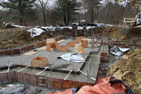 Unlike many Passive House projects, this building has a relatively complex footprint. Here, we see the perimeter basement wall footings already poured, with forms for the interior pad footings distributed around the gravel base inside the home’s footprint.