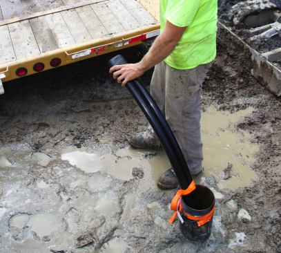 A crew member secures the tubing loop to the well shaft with an optic-orange comealong strap, and seals the ends of the tubes with rubber tape. The well head is now ready for the next step: connecting the ground loop to the house.