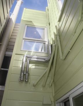 Aluminum cladding protects the insulation on the two pipes that carry fluid to the solar collectors. Slightly lower and to the right are the PVC flue and air intake for the condensing boiler. The hood by the door is the HRV’s air intake.