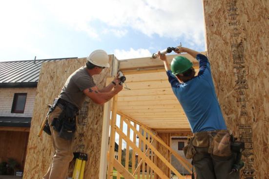 Carpenters apply beads of acrylic sealant to SIPs and stick framing to create an air seal, prior to installing a short section of SIP above a door opening.