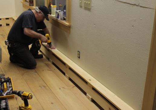 Stock 1x5 boards attach to the blocks in front and the brackets along the wall for the top of the baseboard cover. A small flat trim strip will cover gaps left due to the wavy barn wall.