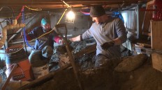 Shane Fenton passes a bucket of concrete to Chris Mitchell in the crawl space. Tight conditions are typical of foundation work in the island's older housing stock.