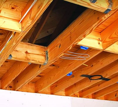 In a typical one-story garage attached to a two-story home, the roof ties into the second-floor walls; in this case, into the knee walls of a much larger attic area. Below the rim joist, the author’s crew hangs drywall on the garage side of the wall, ahead of the drywall crew that will install drywall in the rest of the house.