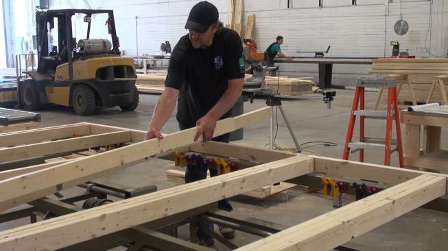 On the shop floor, shop manager Steve Greenleaf sets studs and jacks in place on the precision framing table. At rear, carpenter George Reefer trims wood I-joists to length on the shop’s up-cut saw.