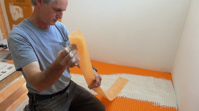 Boucher pre-creases a strip of Kerdi membrane, before mortaring the Kerdi into the corner joint where the Ditra underlayment meets the wall.
