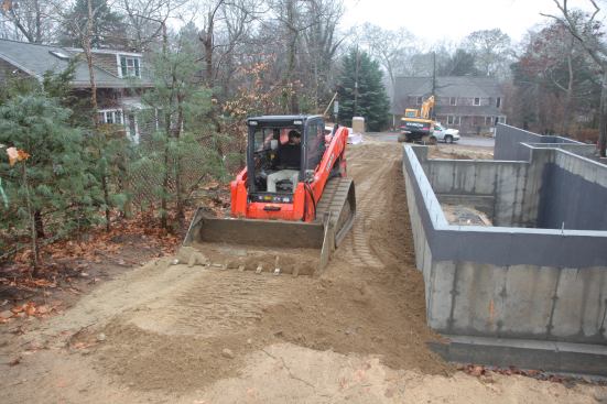 After pushing the fill around the foundation, George uses the bucket of the skid-steer machine to flatten and contour the fill. This allows him to integrate the new slope from the house with the existing slope on the neighboring lot.