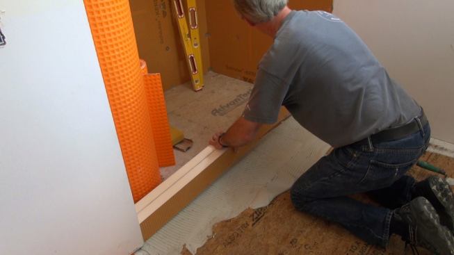 Boucher presses the laminated Kerdi-Board curb down into the mortar bed. Once the cement sets and cures, the curb will be solidly attached.