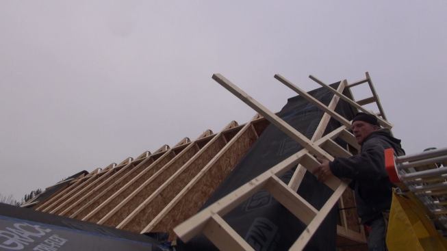 Setting the overhang outrigger on the gable end of the roof. Later, the roof will be strapped, sheathed, and shingled, and finish soffit and fascia trim will be applied to the outrigger.