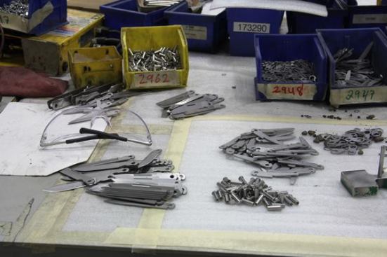 It’s easy to identify the parts at this assembly station; there’s a knife blade, file, and screwdriver. The hollow pieces in the center are rivets. The piece on the right, with the vertical post, is an assembly jig.