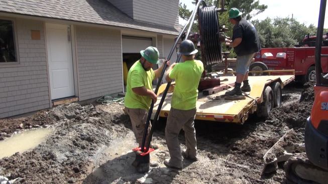 Two crew members guide the tubing into the well shaft while a third unrolls the tubing from a trailer-mounted spindle.
