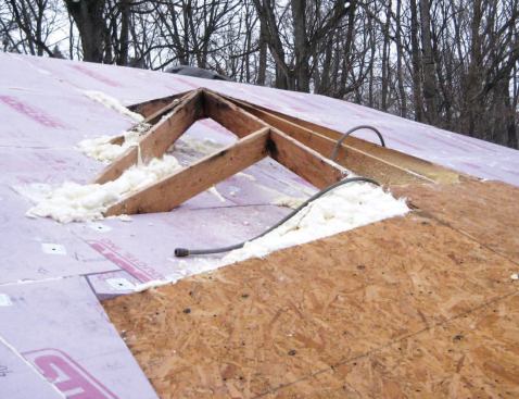 To block air leakage into this cavity, the author cut rigid foam to fit around the framing and over the partially sheathed roof.