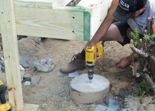 With the deck framing resting on temporary supports, the author lays out and installs the post anchors.