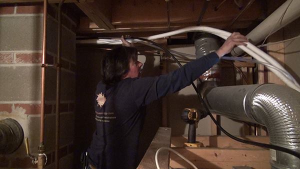 Inside the home’s basement, Chris Blaisdell pulls through the four lines that connect the indoor heating and cooling fan to the outdoor compressor: Two white refrigerant lines (one for vapor and one for liquid refrigerant); a black power and control electrical cable; and a clear condensate line.