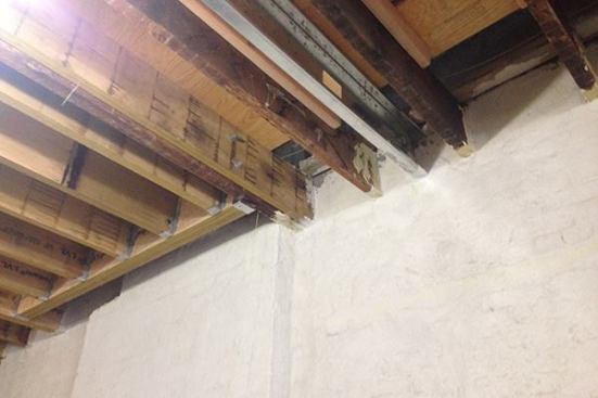 The section of floor at the left of this image needed reinforcing, but the existing brick was connected to the fireplace chimney of the neighboring unit, and could not be disturbed. So contractor Jose Maldonado worked around the area by installing a header and beam system framed with LVL members. At the right of the photo, where the crew was able to tie into the existing brick, a section of floor has been reinforced and levelled with steel C-joists and 2x6 sisters.