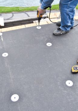 The EPDM installation started with a 1/2-inch-thick fiberboard underlayment engineered to bond with the roofing adhesive. It scores and cuts like cement board and is fastened in place with galvanized screws and washers.