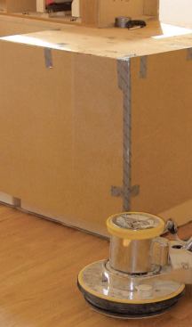 Cabinets are protected with sheets of hardboard secured with duct tape. The bottom edges of the hardboard extend only to the top of the kickspace to permit finishing the floor with the hardboard still in place.